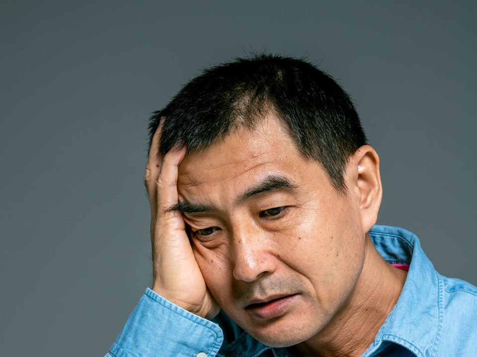 疲れた表情で額に手を当てる男性